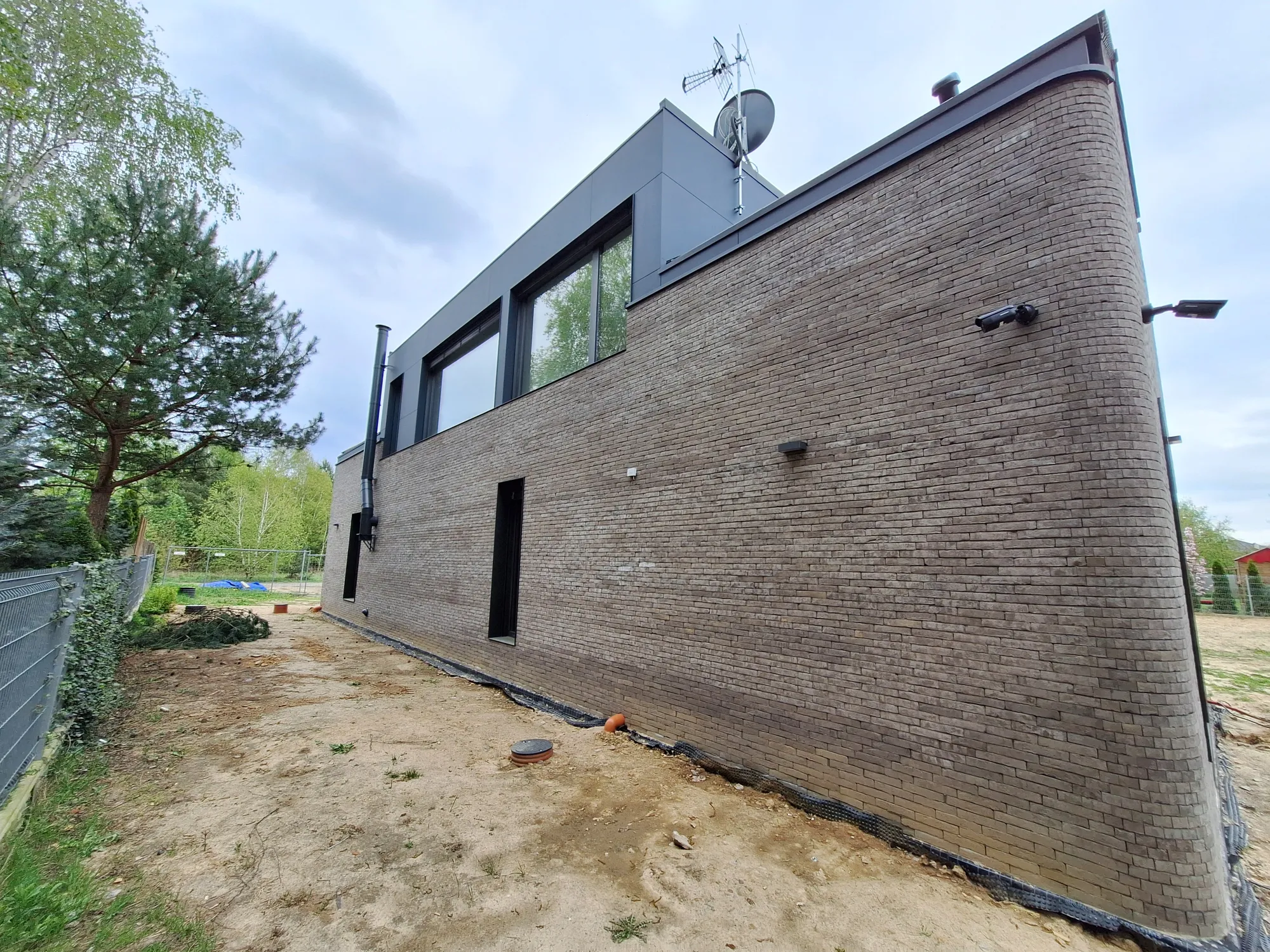 Elewacje nowoczesnego budynku z klinkierową ścianą i przygotowanym terenem wokół