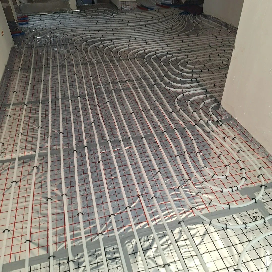 Rury systemu ogrzewania podłogowego ułożone na izolacyjnej folii i metalowej siatce