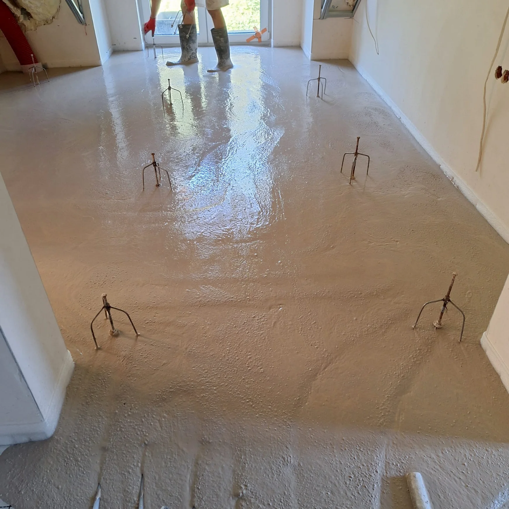 Wylewki anhydrytowe: robotnik w kaloszach rozprowadza masę na podłodze wnętrza budynku