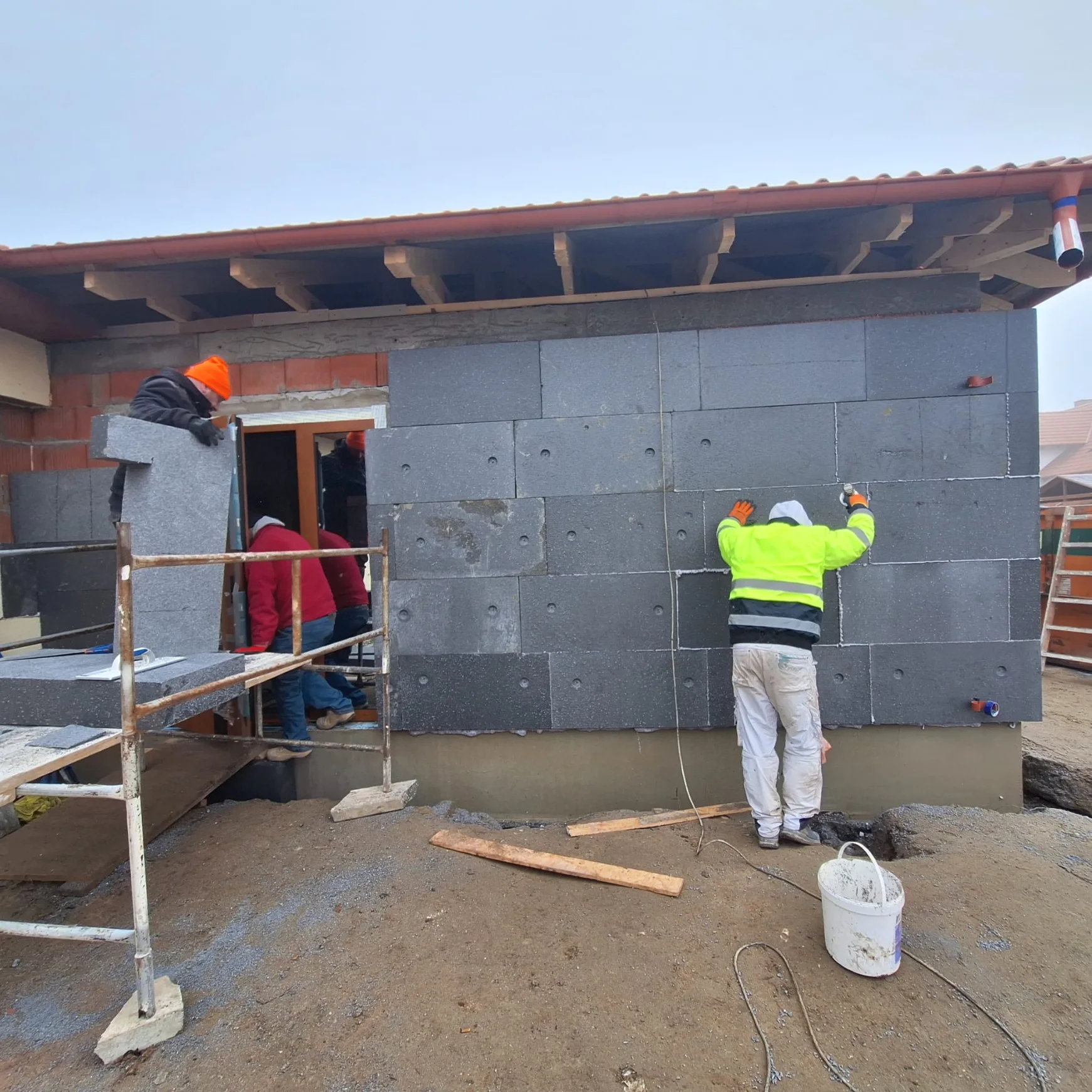 Robotnicy montują płyty izolacyjne na elewacji w ramach Ocieplenia budynków