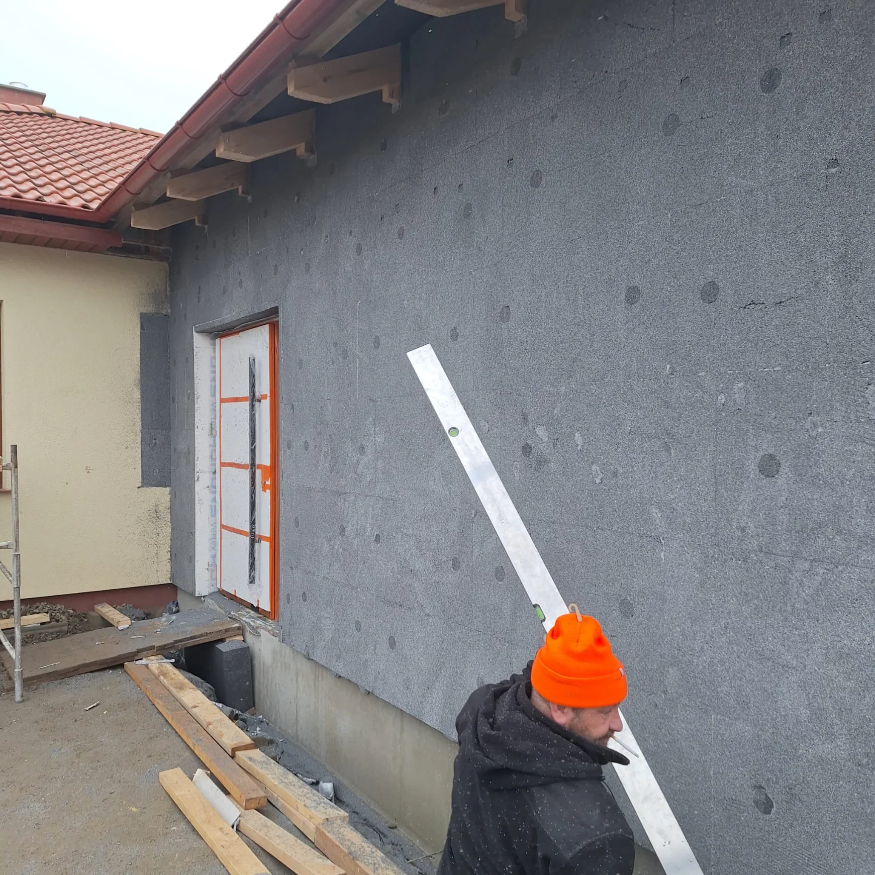 Monter sprawdza poziomicą ułożenie zewnętrznej izolacji ścian – ocieplenia budynków